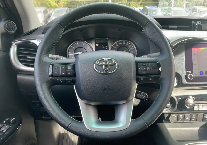 Vue rapprochée du volant multifonction noir du Toyota Hilux 2025, tableau de bord et écran tactile visibles.