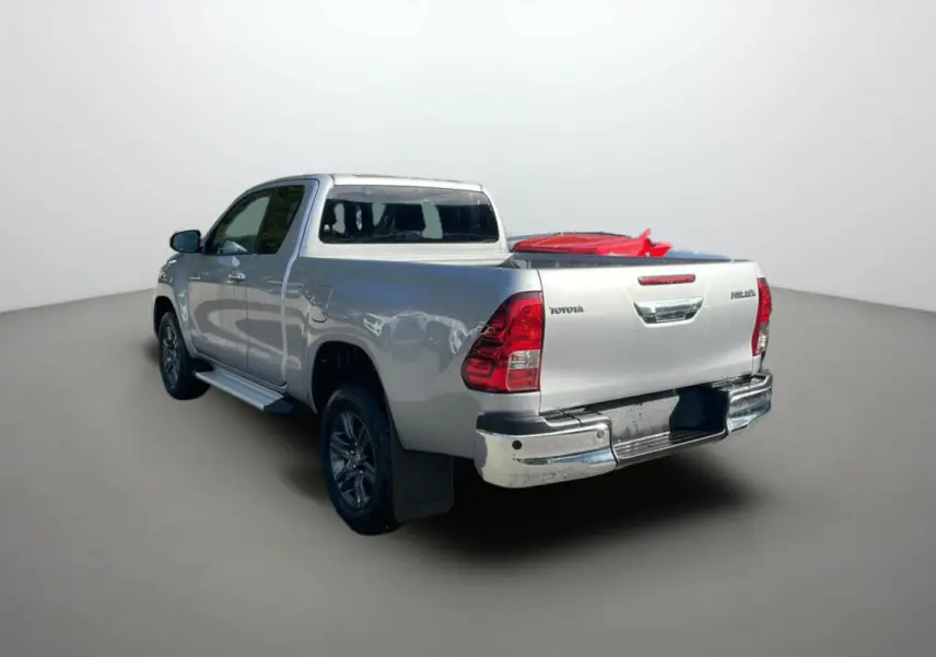 Toyota Hilux 4x4 gris acier vu en 3/4 arrière droit, avec benne chargée et détails chromés sur pare-chocs.