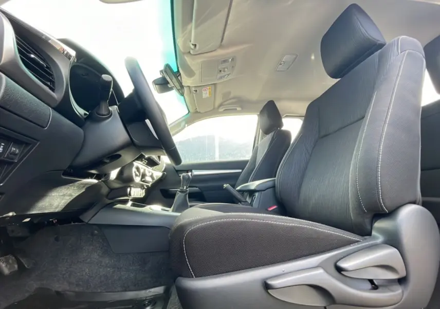 Intérieur du Toyota Hilux 2025 gris acier, vue côté conducteur montrant sièges et tableau de bord avec boîte manuelle.