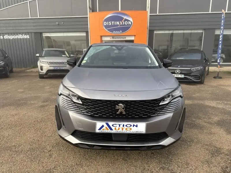 Vue frontale d'un Peugeot 3008 gris Artense avec calandre noire et logo lion au centre, stationné devant un concessionnaire.