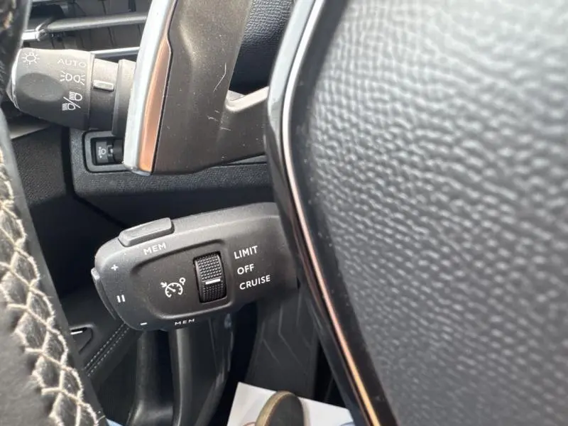 Gros plan sur la commande de régulateur de vitesse à gauche du volant cuir du Peugeot 3008 gris Artense 2022.