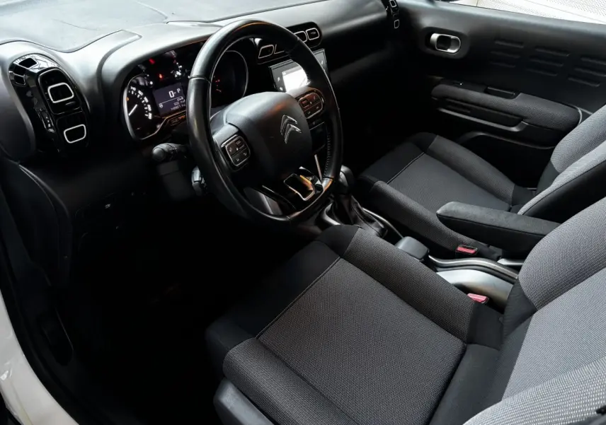 Vue intérieure côté conducteur du Citroën C3 Aircross blanc 2021, avec volant multifonctions et sièges tissu gris.