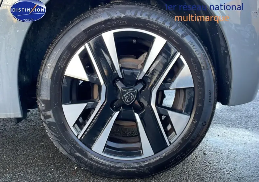 Gros plan sur la jante alu noire et argentée d'une Peugeot 208 gris sélénite, avec logo Peugeot au centre.