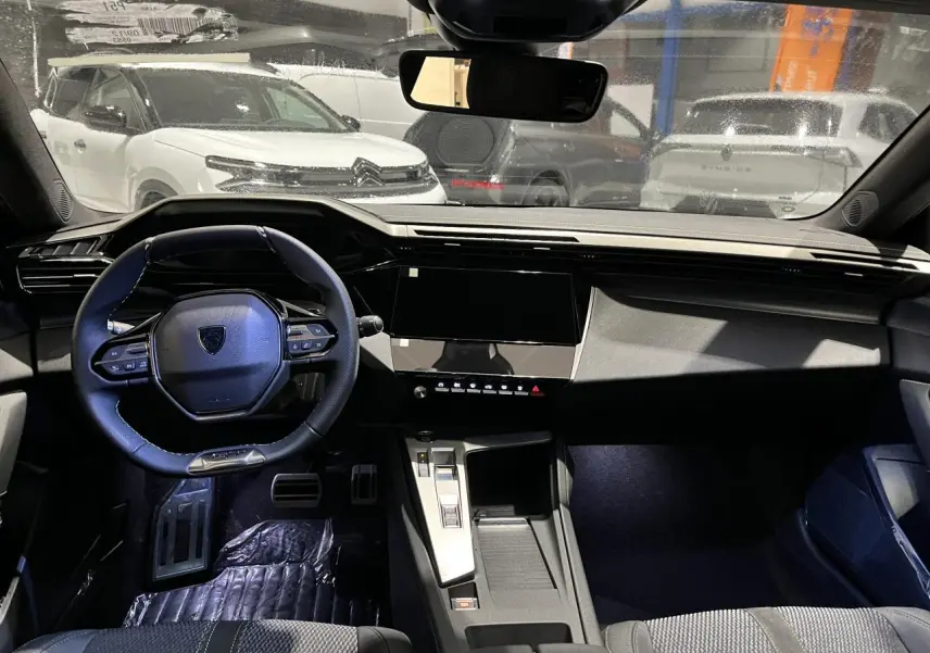 Vue intérieure avant de la Peugeot 308 2024 gris Artense, volant cuir, planche de bord moderne et écran tactile noir.