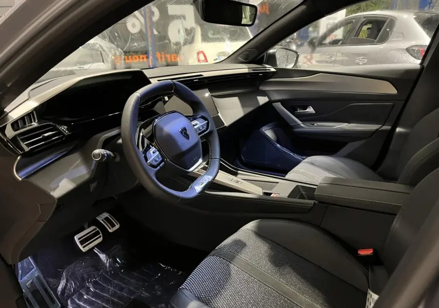 Vue intérieure côté conducteur de la Peugeot 308 GT 2024, avec volant cuir, sellerie tri-matières et planche de bord noire.