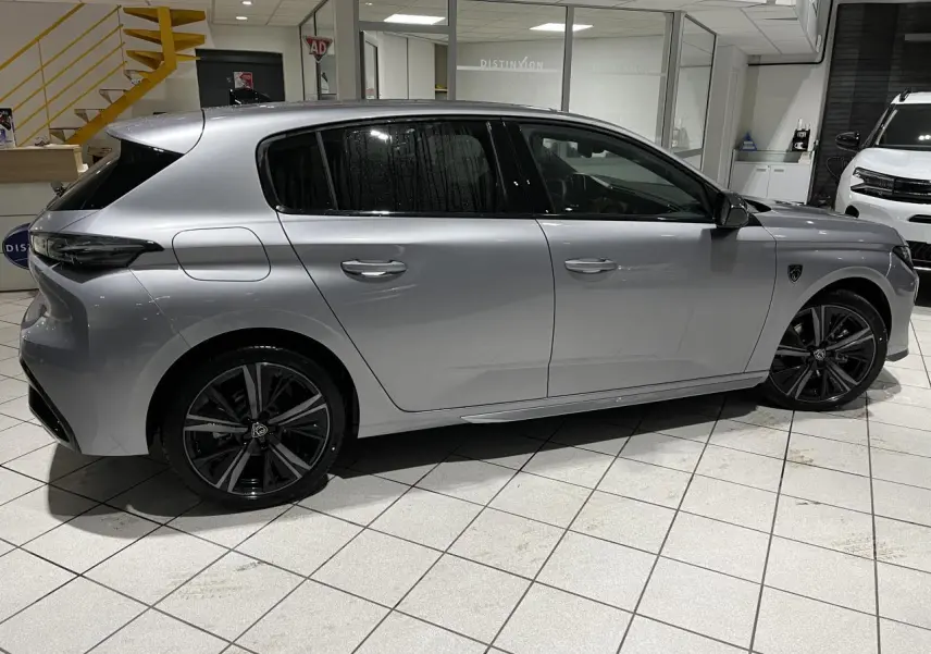 Peugeot 308 Gris Artense vue de profil côté gauche en intérieur, jantes alliage noires et vitres surteintées.