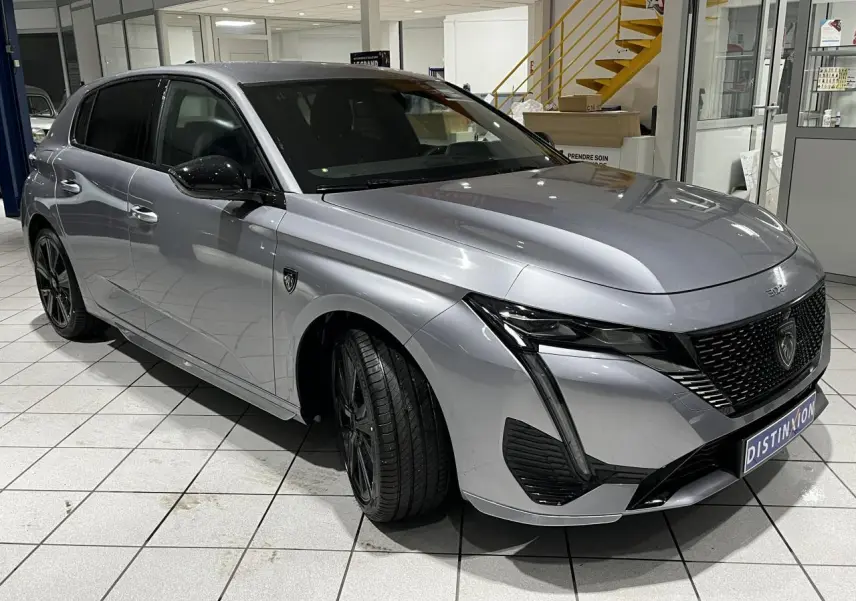 Peugeot 308 GT gris Artense vue 3/4 avant en intérieur avec calandre noire et jantes alliage 18 pouces.