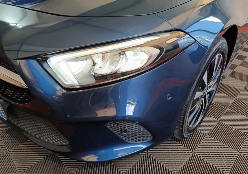 Gros plan sur l'avant droit bleu d'une Mercedes Classe A 250 e Business Line avec phare LED et jante alliage.