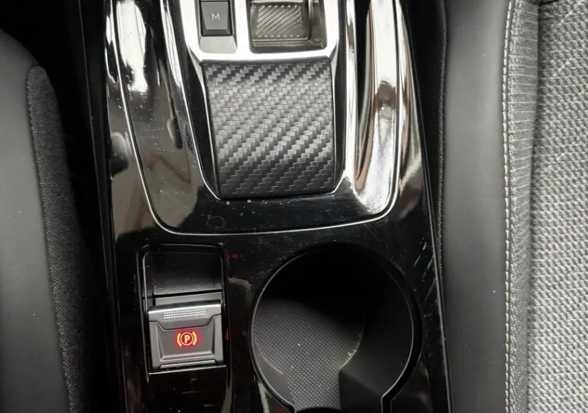 Vue rapprochée de la console centrale noire brillante du Peugeot 2008 Hybrid 145, avec sélecteur de vitesse et porte-gobelets.