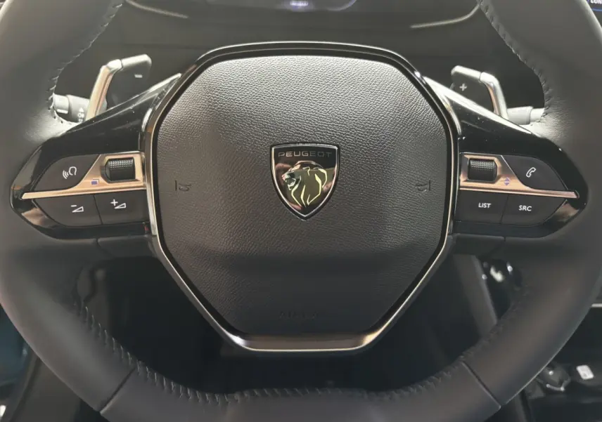 Gros plan sur le volant cuir noir du Peugeot 2008 Hybrid 145, avec commandes multifonctions et logo lion central.