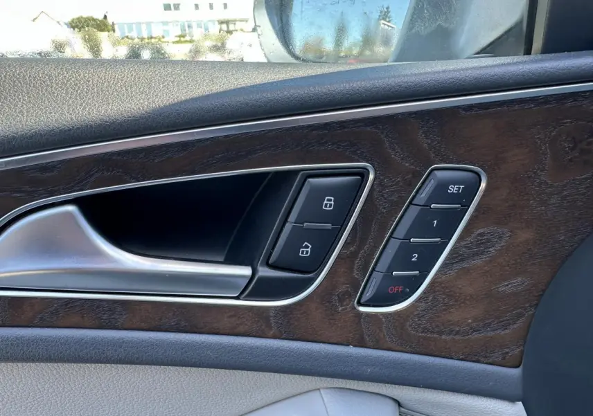 Gros plan sur la porte intérieure côté gauche d’une Audi A6 2015 avec insert bois et commandes de verrouillage et mémoire sièges.