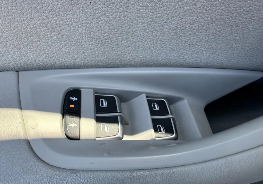 Gros plan sur les commandes de lève-vitres et verrouillage enfant sur la porte intérieure grise d'une Audi A6 2015.