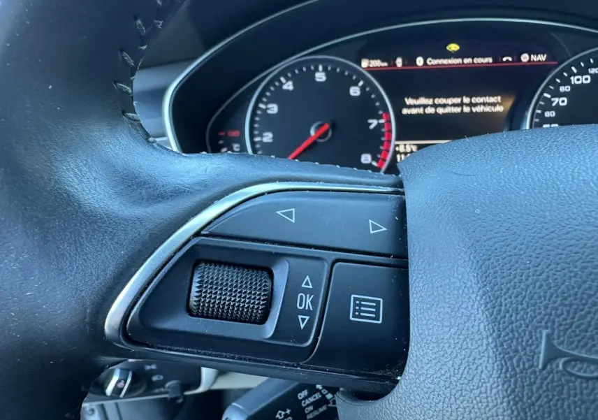 Gros plan sur les commandes gauche du volant cuir d’une Audi A6 2.0 TFSI 2015 avec tableau de bord numérique.