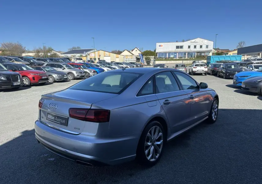Audi A6 gris vue 3/4 arrière droit sur parking avec jantes aluminium et feux arrière foncés.