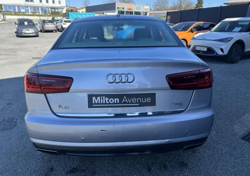 Vue arrière d'une Audi A6 gris métallisé avec logo et badges TFSI, stationnée sur un parking extérieur.