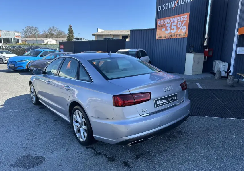Audi A6 gris vue 3/4 arrière droit, avec feux arrière LED et double sortie d’échappement chromée.