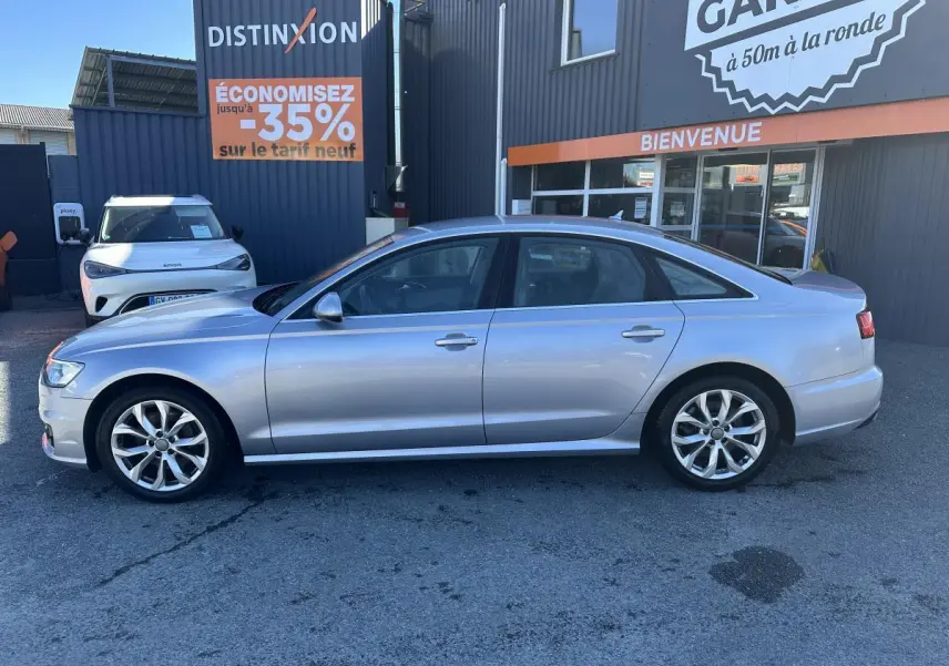 Audi A6 gris en profil droit, garée devant un bâtiment commercial avec enseigne "Distinxion".