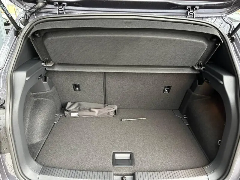 Vue intérieure du coffre ouvert d'un Volkswagen T-Cross 1.0 TSI 116ch R-Line 2026, avec tapis gris et cache-bagages relevé.