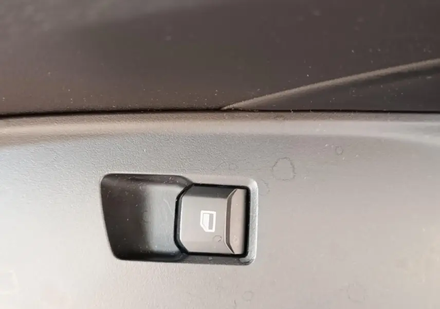 Gros plan sur le bouton de commande de lève-vitre intérieur, plastique noir, dans une MG3 2024 gris foncé.