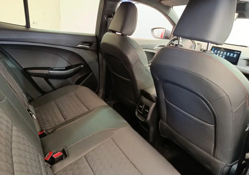Vue intérieure arrière côté droit du MG3 2024, sièges noirs avec surpiqûres rouges et écran tactile avant visible.