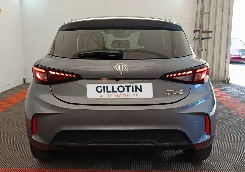 Vue arrière d'une MG3 gris foncé avec feux LED allumés et logo MG visible sur un sol à damiers rouges et gris.