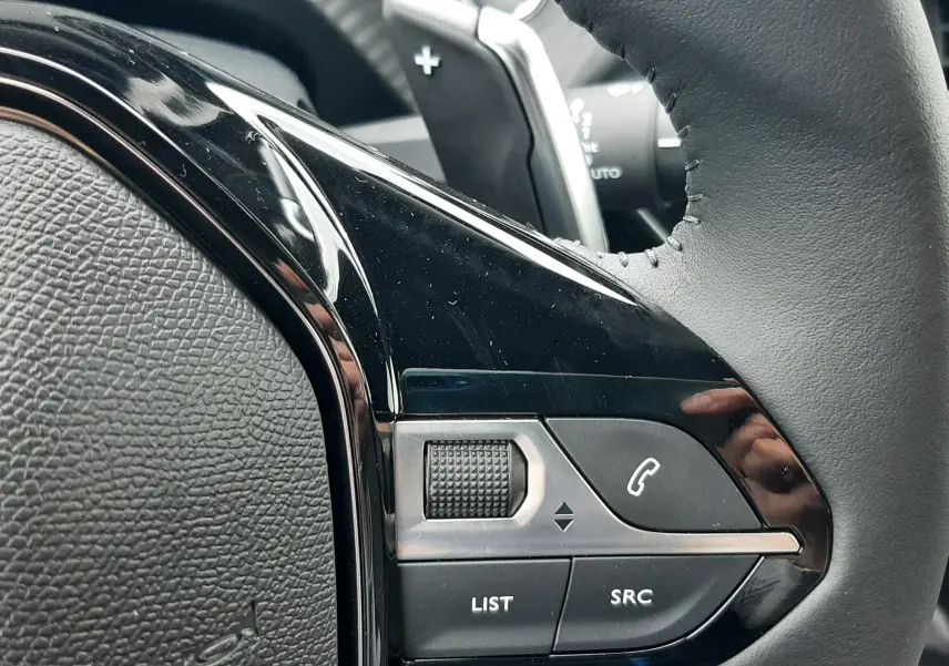 Gros plan sur les commandes noires du volant en cuir du Peugeot 2008 gris Artense, version hybride 2025.