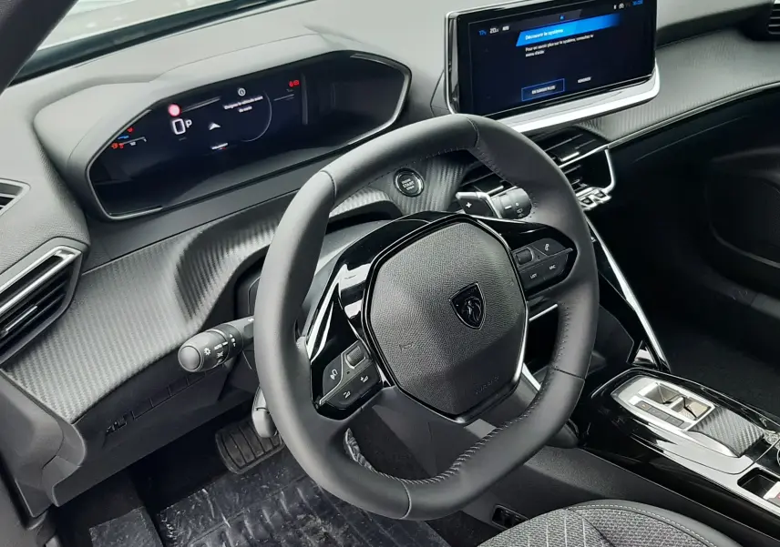 Vue intérieure du tableau de bord et volant noir du Peugeot 2008 hybride 2025 avec écran tactile et sellerie grise.
