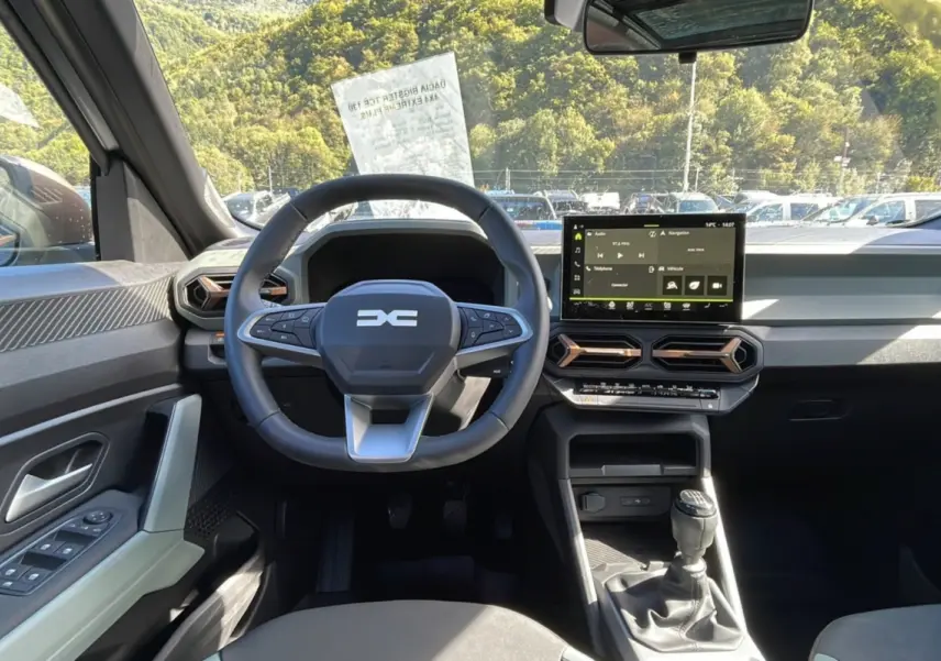 Intérieur du Dacia Bigster 2025 essence gris schiste, vue frontale du poste de conduite avec volant et écran tactile.
