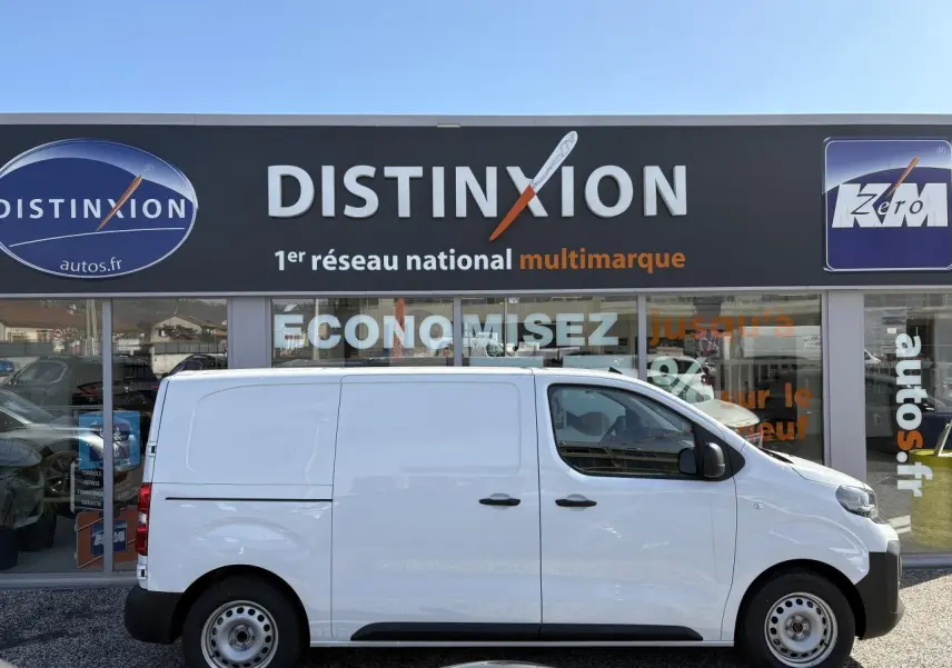 Profil droit d’un utilitaire Opel Vivaro blanc 2024 stationné devant une concession Distinxion.