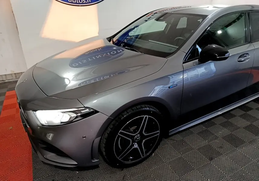 Mercedes Classe A 250 e AMG Line gris foncé vue 3/4 avant droit, avec jantes noires et phares LED allumés.