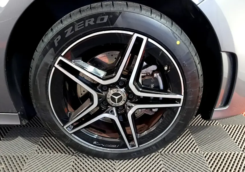Gros plan sur la jante AMG noire et argentée avec logo Mercedes, montée sur pneu Pirelli P Zero, carrosserie gris foncé visible.