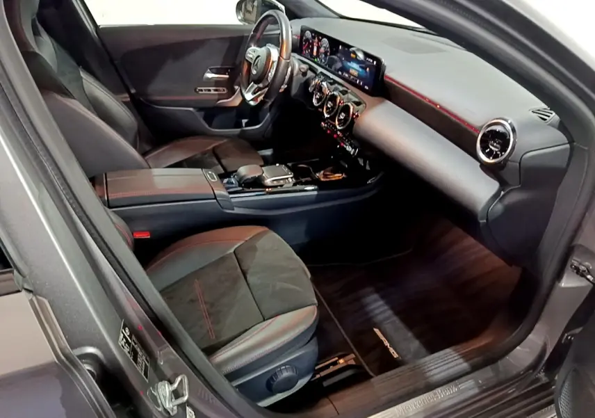 Vue intérieure côté conducteur de la Mercedes Classe A 250 e AMG Line 2021, sièges noirs avec surpiqûres rouges et tableau de bord numérique.