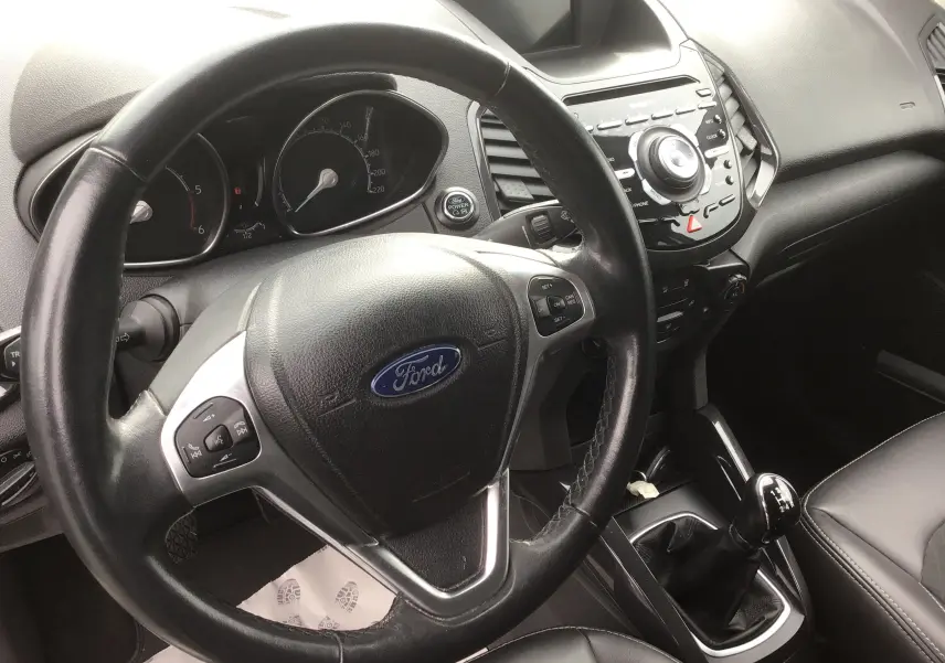 Vue intérieure centrée sur le volant Ford et la console centrale noire du Ford Ecosport gris foncé, avec levier de vitesse manuel visible.