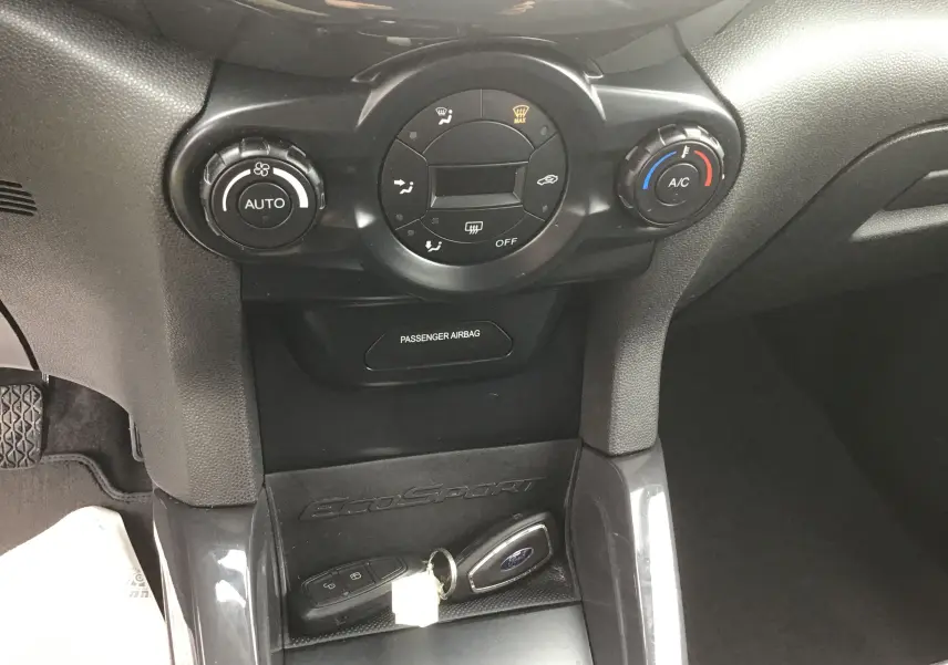 Vue rapprochée du tableau de bord central du Ford EcoSport gris foncé, avec commandes de climatisation et clés mains libres posées.