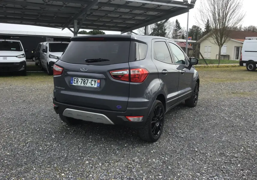 Vue 3/4 arrière droite d'un Ford EcoSport gris foncé métallisé avec jantes noires et vitres teintées, stationné sur gravier.