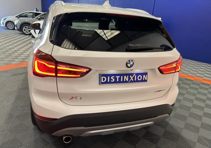 Vue arrière droite d'un BMW X1 blanc avec feux allumés et hayon électrique dans un showroom.