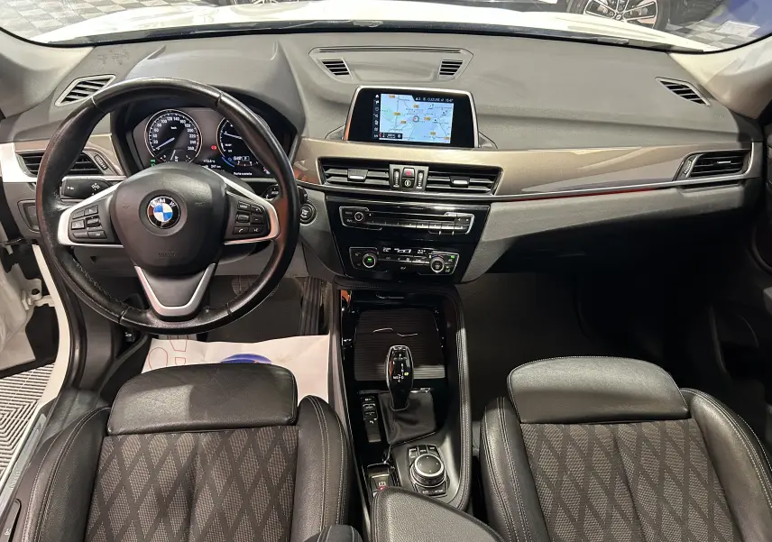 Vue intérieure avant de la BMW X1 sDrive18iA 2018, tableau de bord avec écran GPS et volant multifonction en cuir noir.