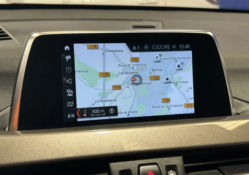 Écran de navigation GPS intégré au tableau de bord beige d'une BMW X1 blanche, vue intérieure frontale.