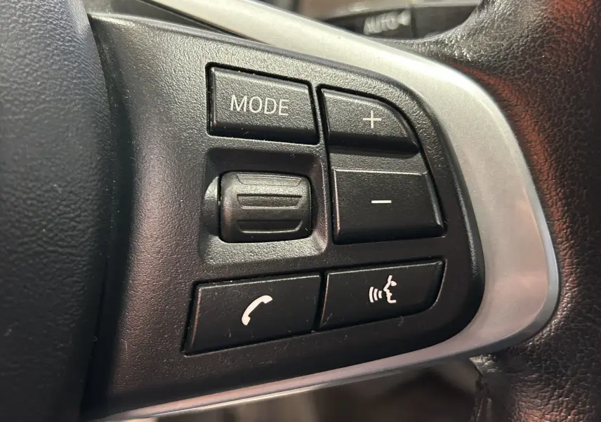 Gros plan sur les boutons de commande au volant côté gauche du BMW X1 blanc, avec touches mode, volume et téléphone.