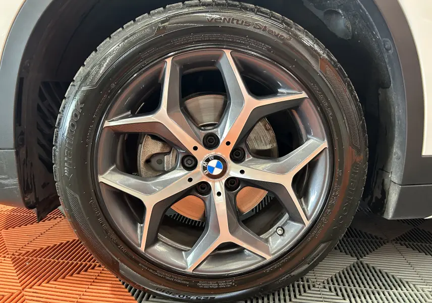 Gros plan sur la jante avant droite en alliage gris foncé du BMW X1 blanc, avec logo BMW au centre.