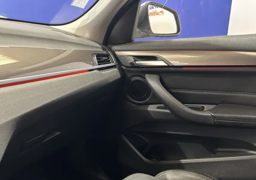 Vue intérieure côté passager du BMW X1 blanc 2018, mettant en valeur la garniture noire avec insert rouge et la poignée de porte.