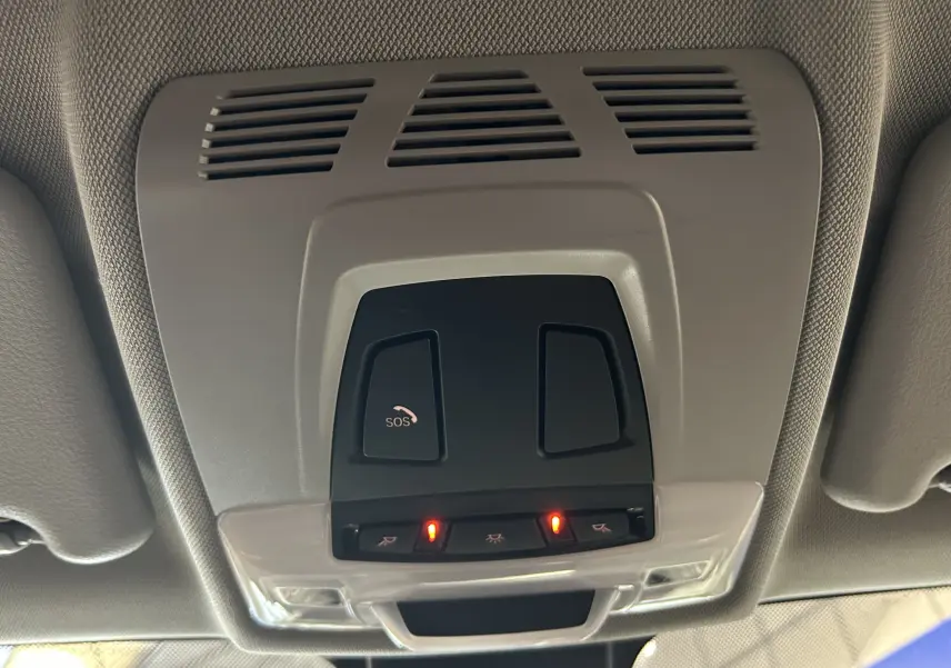 Vue en gros plan du plafonnier intérieur gris avec boutons SOS et éclairage activé dans un BMW X1 blanc 2018.