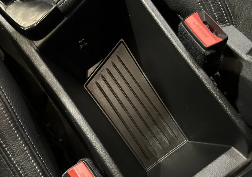 Vue rapprochée de la console centrale noire avec port USB et ceinture de sécurité rouge dans un BMW X1 blanc 2018.