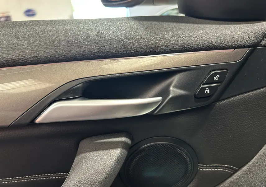 Poignée intérieure côté gauche de la porte avant d'une BMW X1 blanche, avec boutons de verrouillage et haut-parleur visible.