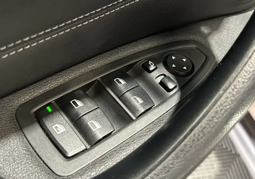 Gros plan sur les commandes de lève-vitres et réglage des rétroviseurs côté conducteur d'un BMW X1 blanc de 2018.