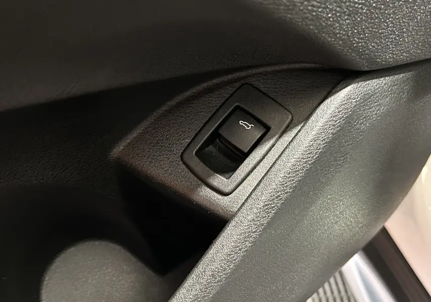 Gros plan sur le bouton d'ouverture électrique du hayon dans l'habitacle d'un BMW X1 blanc.
