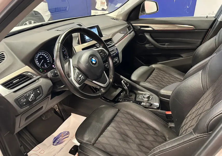 Vue intérieure côté conducteur du BMW X1 sDrive18iA 2018, avec sièges noirs et tableau de bord moderne.