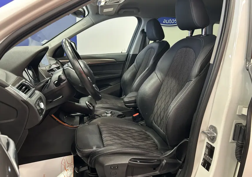 Vue intérieure côté conducteur d'un BMW X1 blanc 2018, sièges avant en cuir noir avec surpiqûres contrastantes.