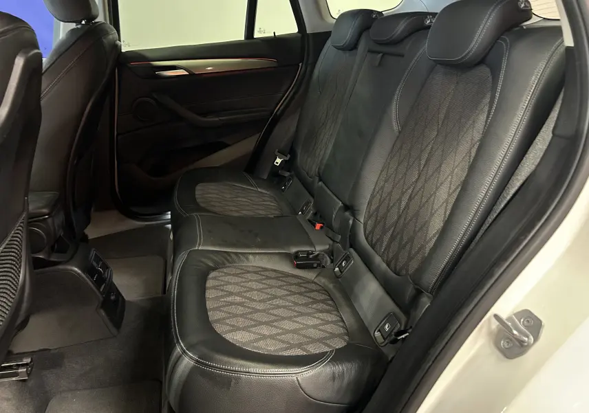 Vue intérieure côté droit des sièges arrière en cuir noir et tissu à motifs d'un BMW X1 blanc de 2018 avec porte ouverte.