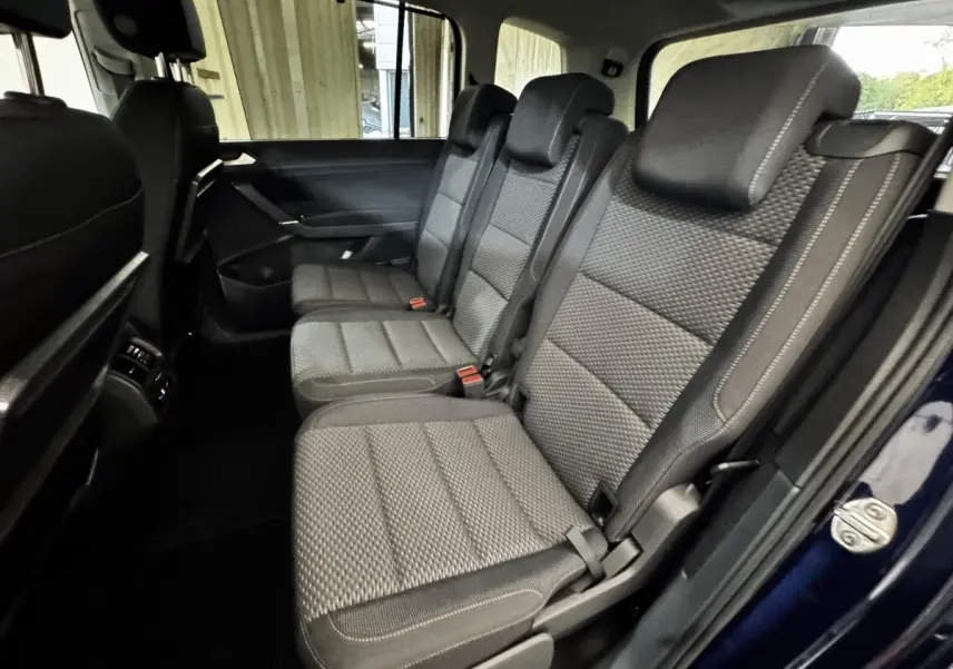 Vue intérieure côté droit sur la deuxième rangée de sièges gris du Volkswagen Touran 2024 bleu, version 7 places.